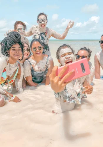 Un grupo de amigos joviales tomando un selfie en la playa con arena en sus rostros y ropa, destacando su felicidad y unión.