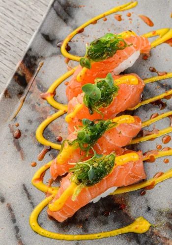 Imagen de una delicada presentación de sushi de salmón adornado con salsa de mango y hierbas frescas, servido en Mix Restaurant & Bar.